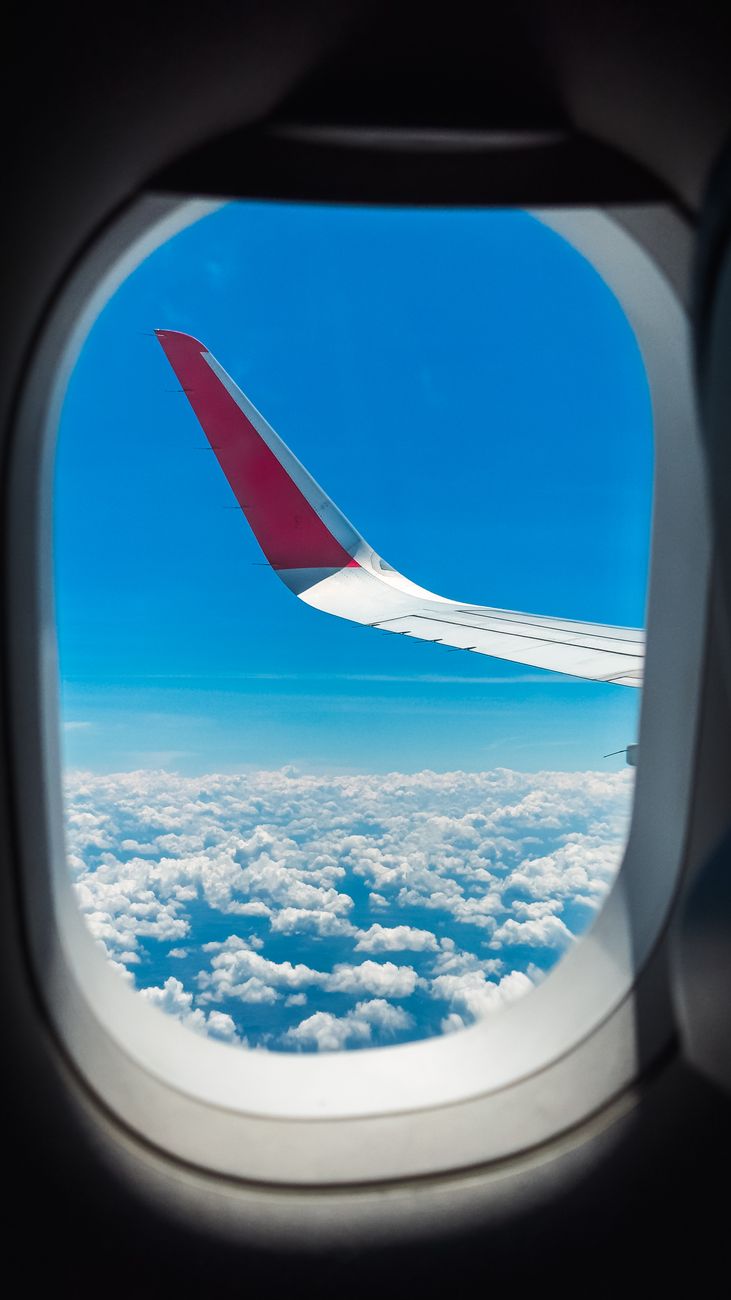wing sky and clouds behind window of flying airplane